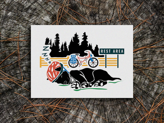 Art print of a black dog sleeping with a helmet on and a bike and trees in the background.