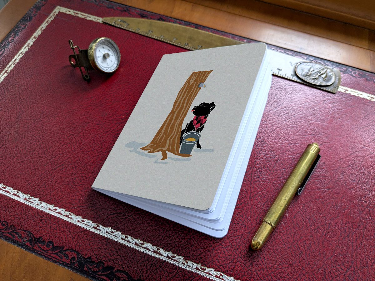 Notebook with illustration of a dog at maple syrup tap on a red desk.