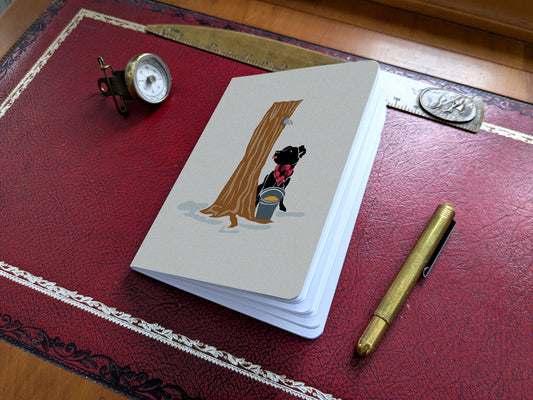 Notebook with illustration of a dog at maple syrup tap on a red desk.