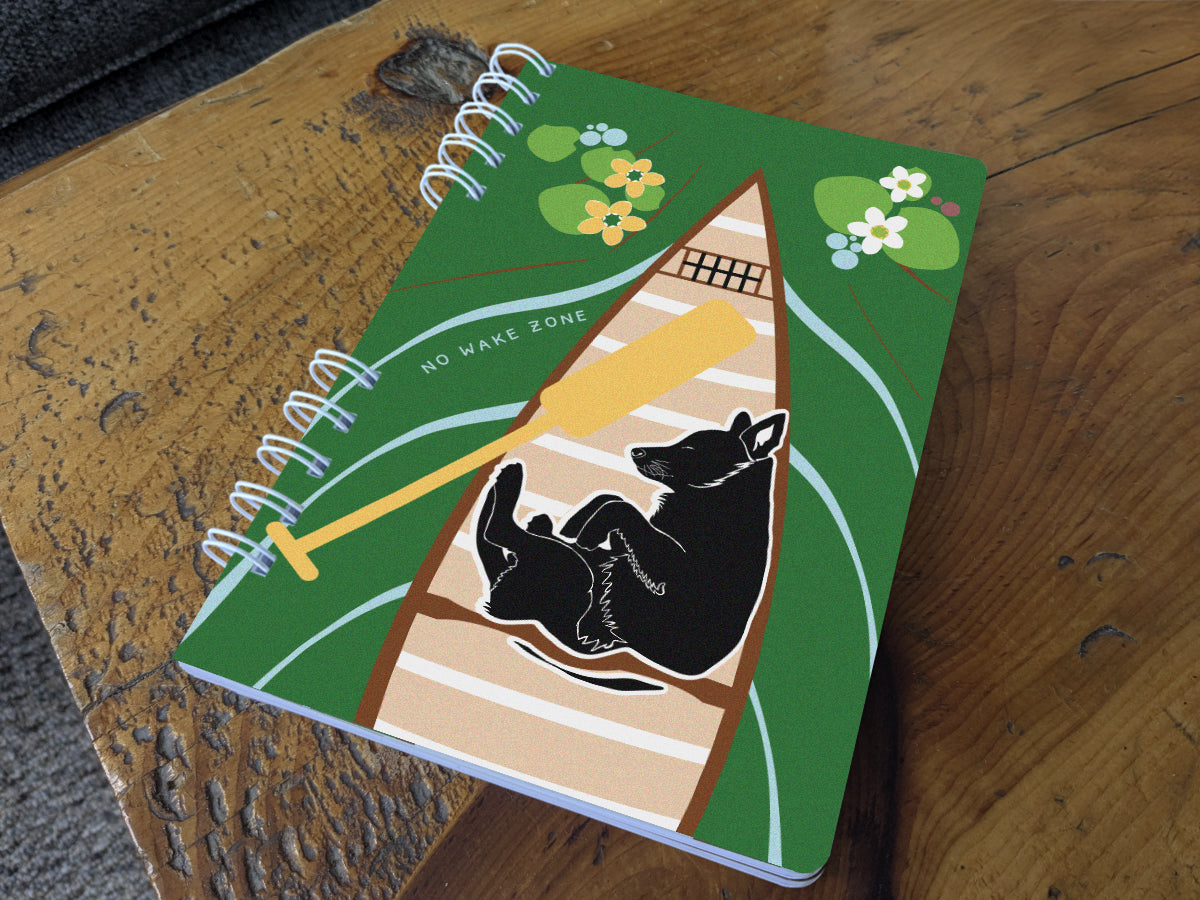 Notebook with illustration of dog sleeping in a canoe with text No Wake Zone on a table.