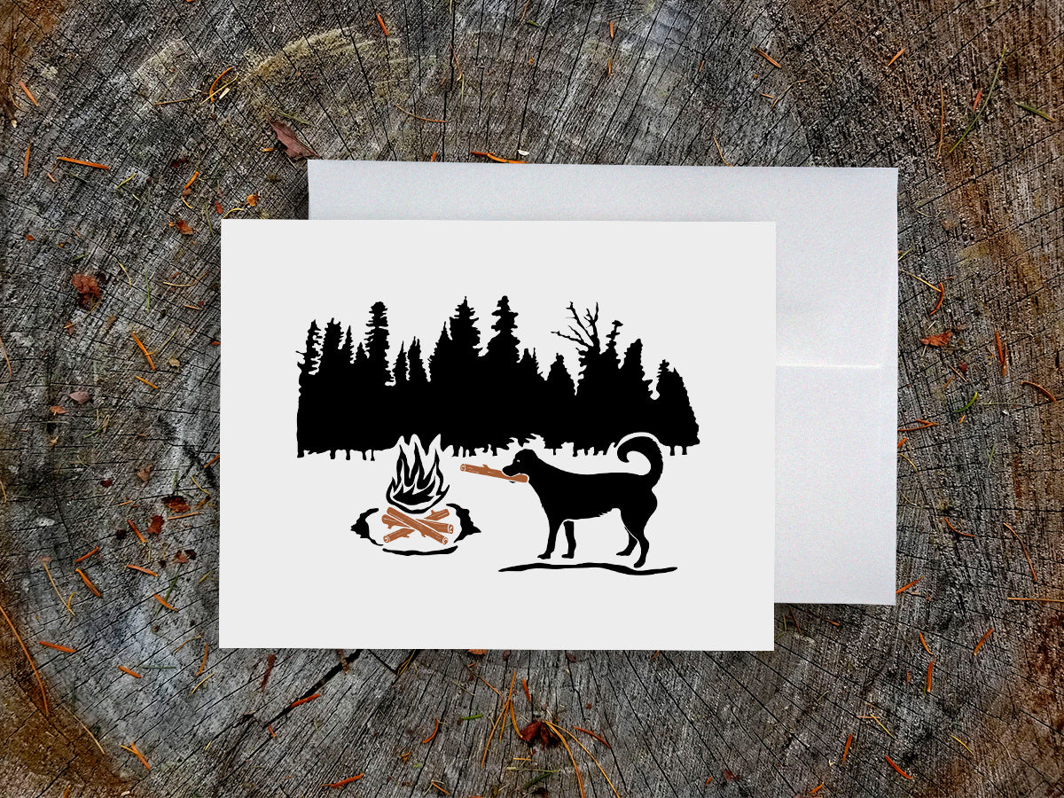 Greeting card of black dog putting a log in a campfire with forest background.