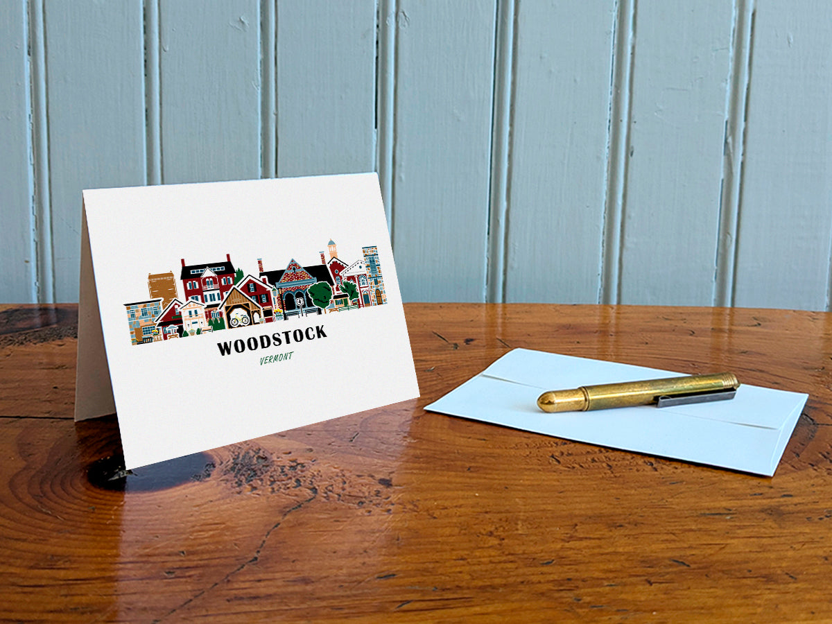Greeting card with Woodstock, Vermont design on a wooden table with an envelope and pen.