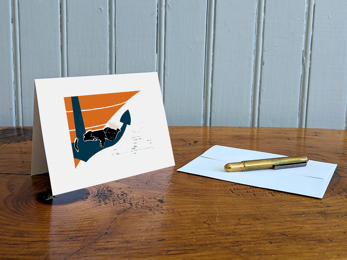 Greeting card with image of a dog sleeping on an anchor on a table with gold pen and envelope.