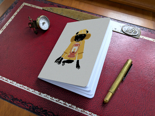 Notebook with illustration of a dog in fisherman yellow jacket with lamp on a red desk.
