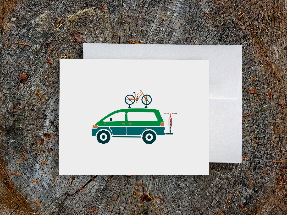 Greeting card with a blue and green van carrying two bikes with wood background