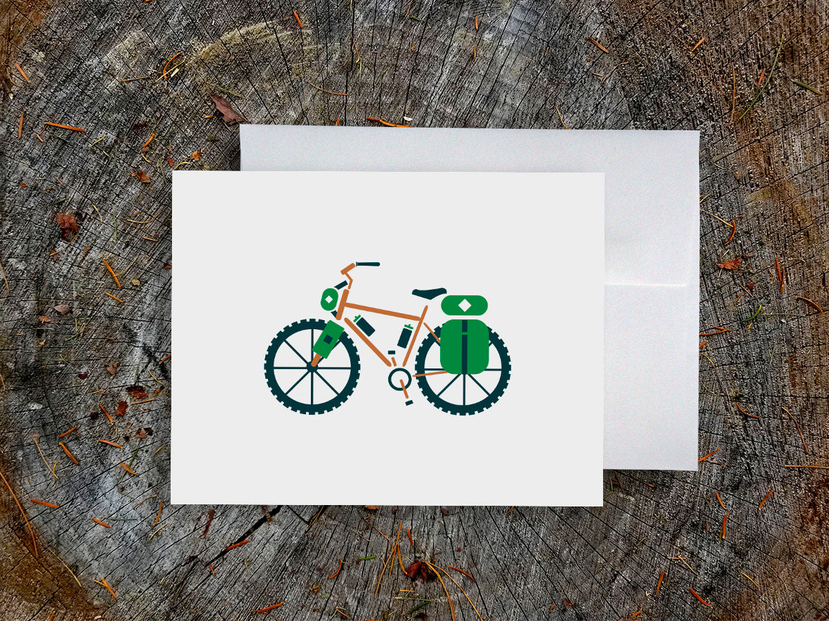 Greeting card with an orange bike with green travel bags with wood background