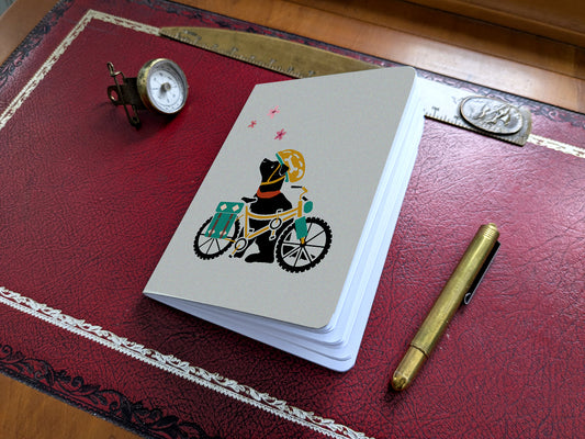 Notebook with illustration of a dog with helmet and bike on a red desk.