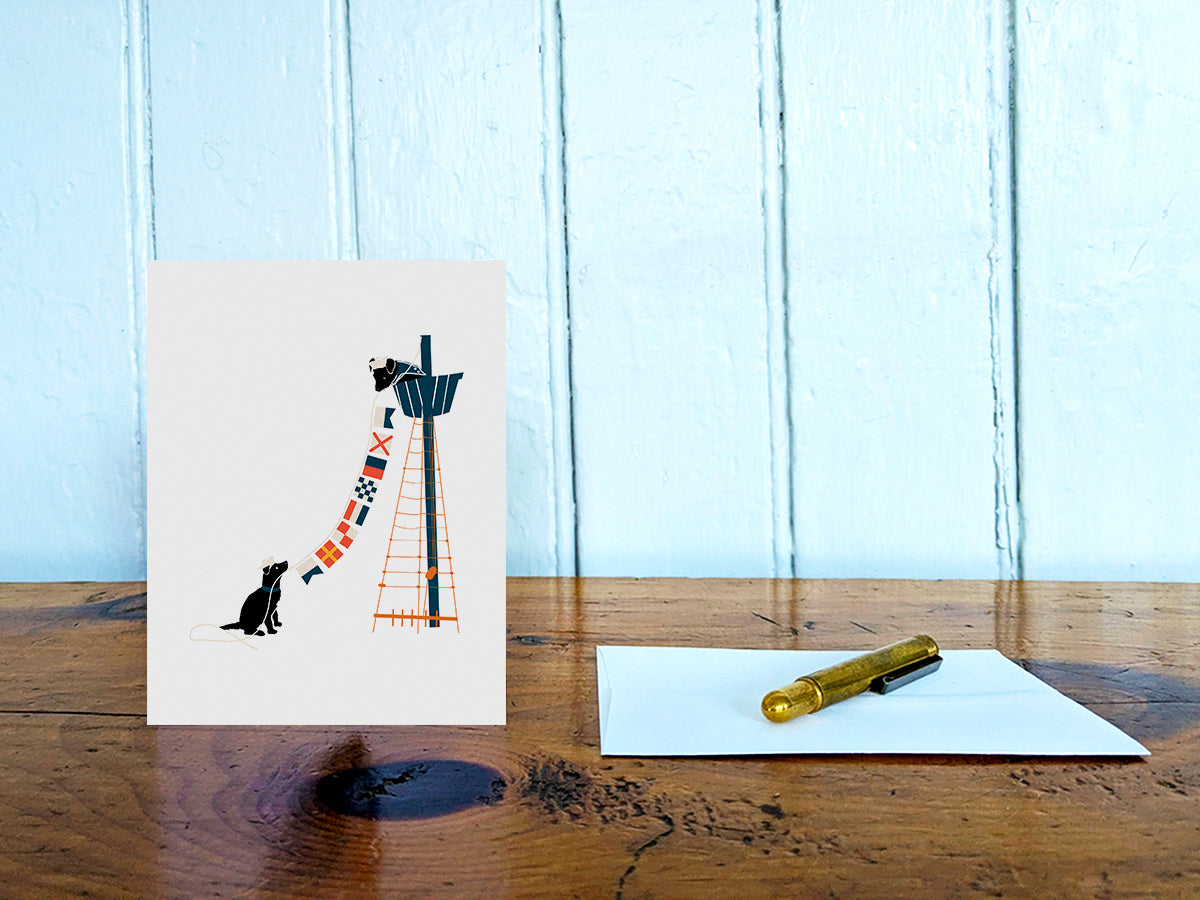 Greeting card with image of two dogs hanging nautical flags on a table with gold pen and envelope.