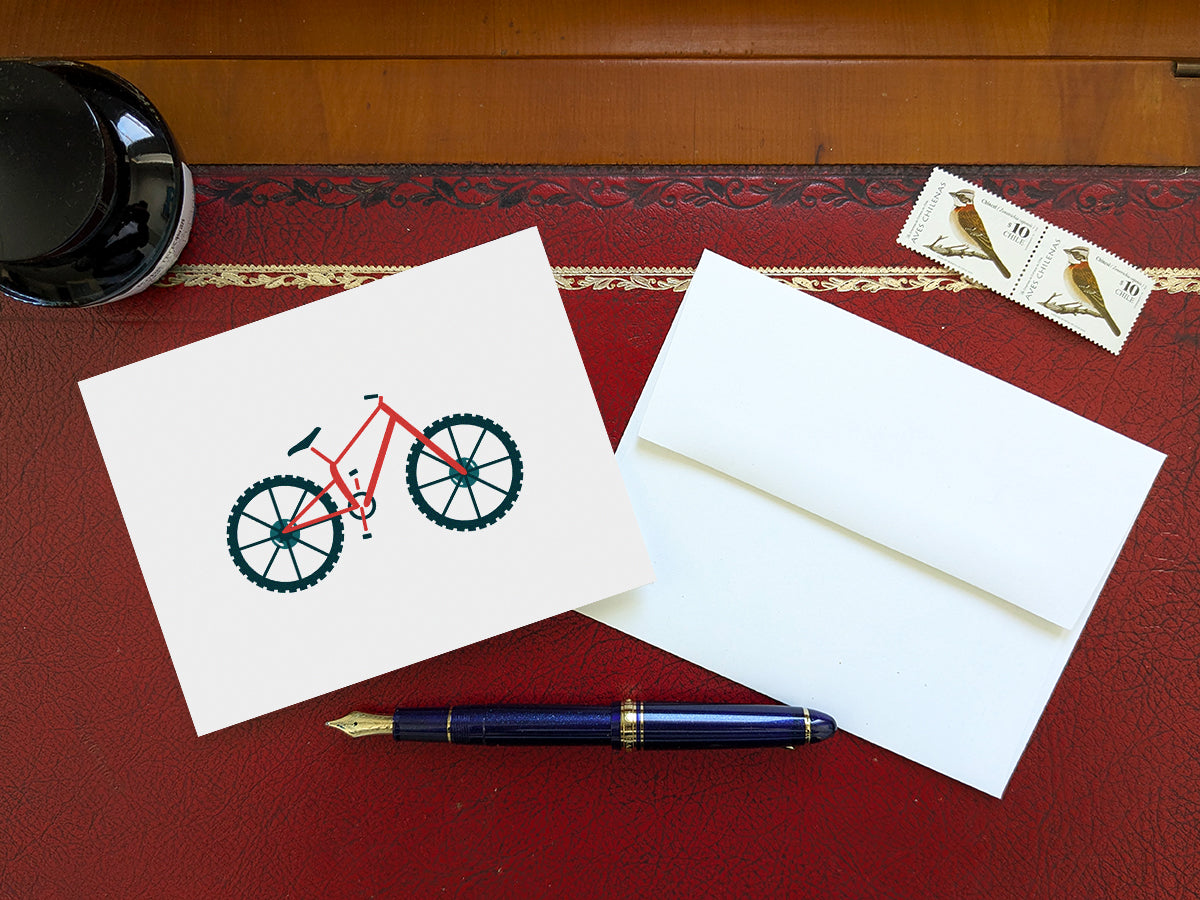 Greeting card with a red mountain bike with basket on a table with a blue pen and envelope and stamps