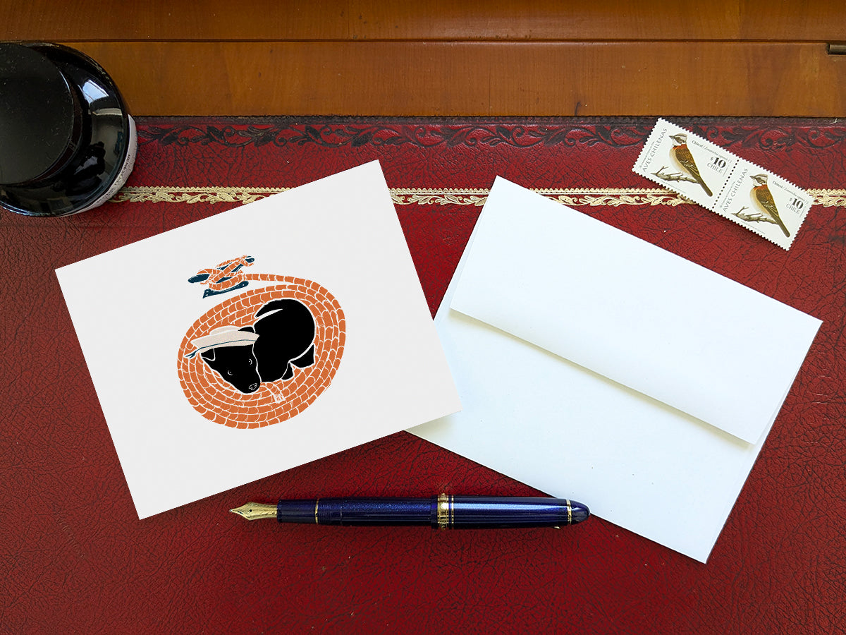 Greeting card with image of a dog with a sailor hat surrounded by rope on a table with a blue pen and envelope and stamps.