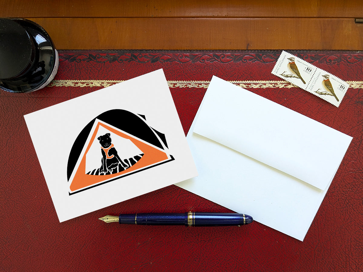 Greeting card with black dog with orange harness sitting in an orange camping tent on a table with blue pen and envelope and stamps.
