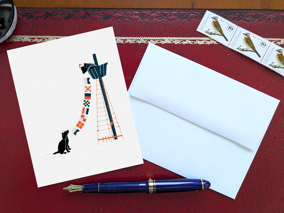 Greeting card with image of two dogs hanging nautical flags on a table with a blue pen and envelope and stamps.