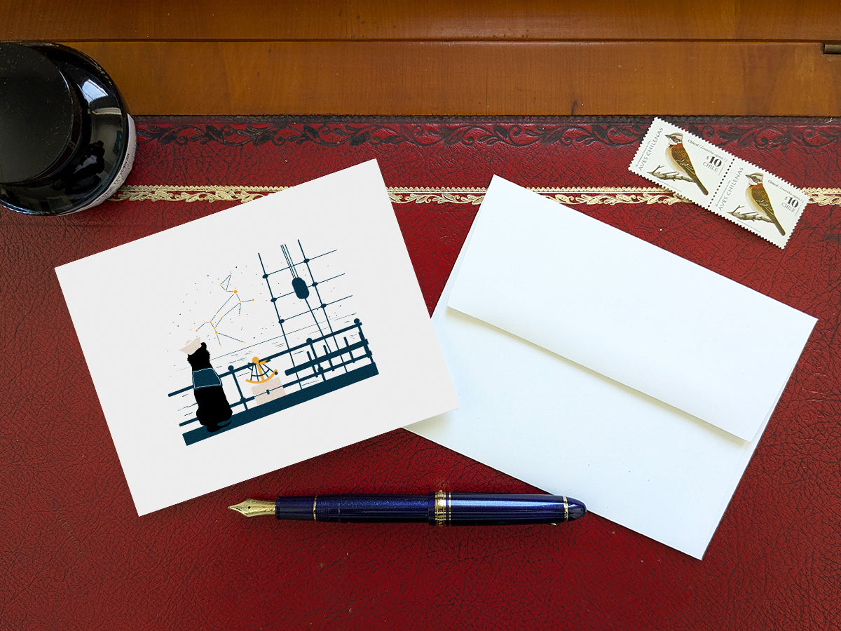 Greeting card with image of a dog with a sextant looking at the stars on a table with a blue pen and envelope and stamps.