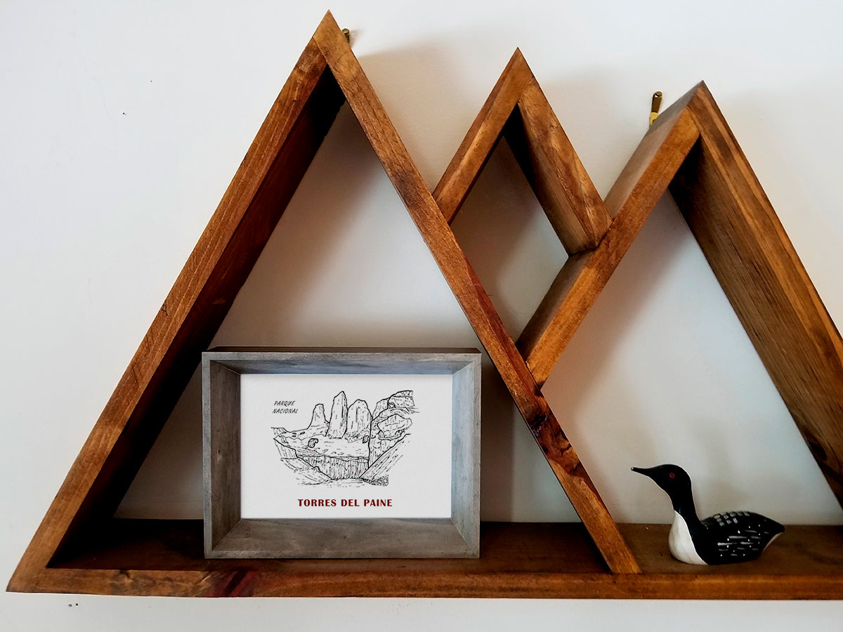 Framed art print on a wooden shelf of black and white mountains and the text Parque Nacional Torres del Paine