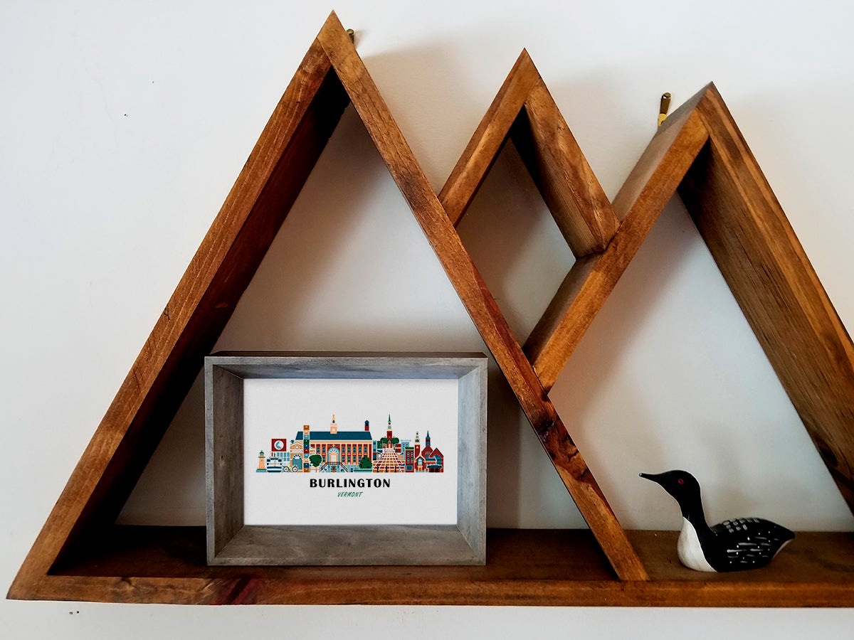 Framed art print on a wooden shelf of buildings arranged in a skyline with the text Burlington Vermont
