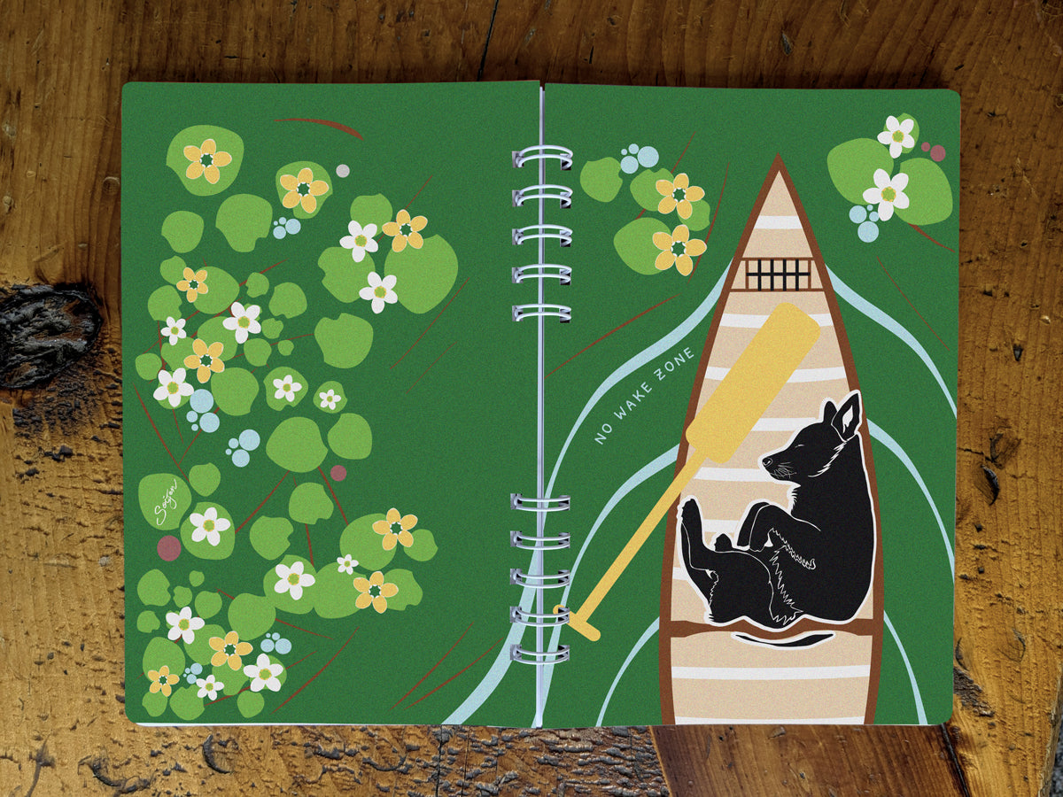 Notebook with illustration of dog sleeping in a canoe with text No Wake Zone on a table.