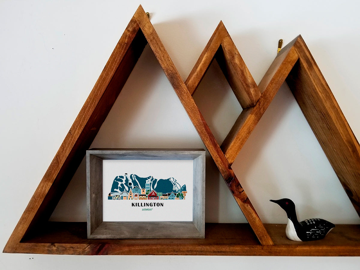 Framed art print on a wooden shelf of buildings arranged in a skyline with the text Killington Vermont