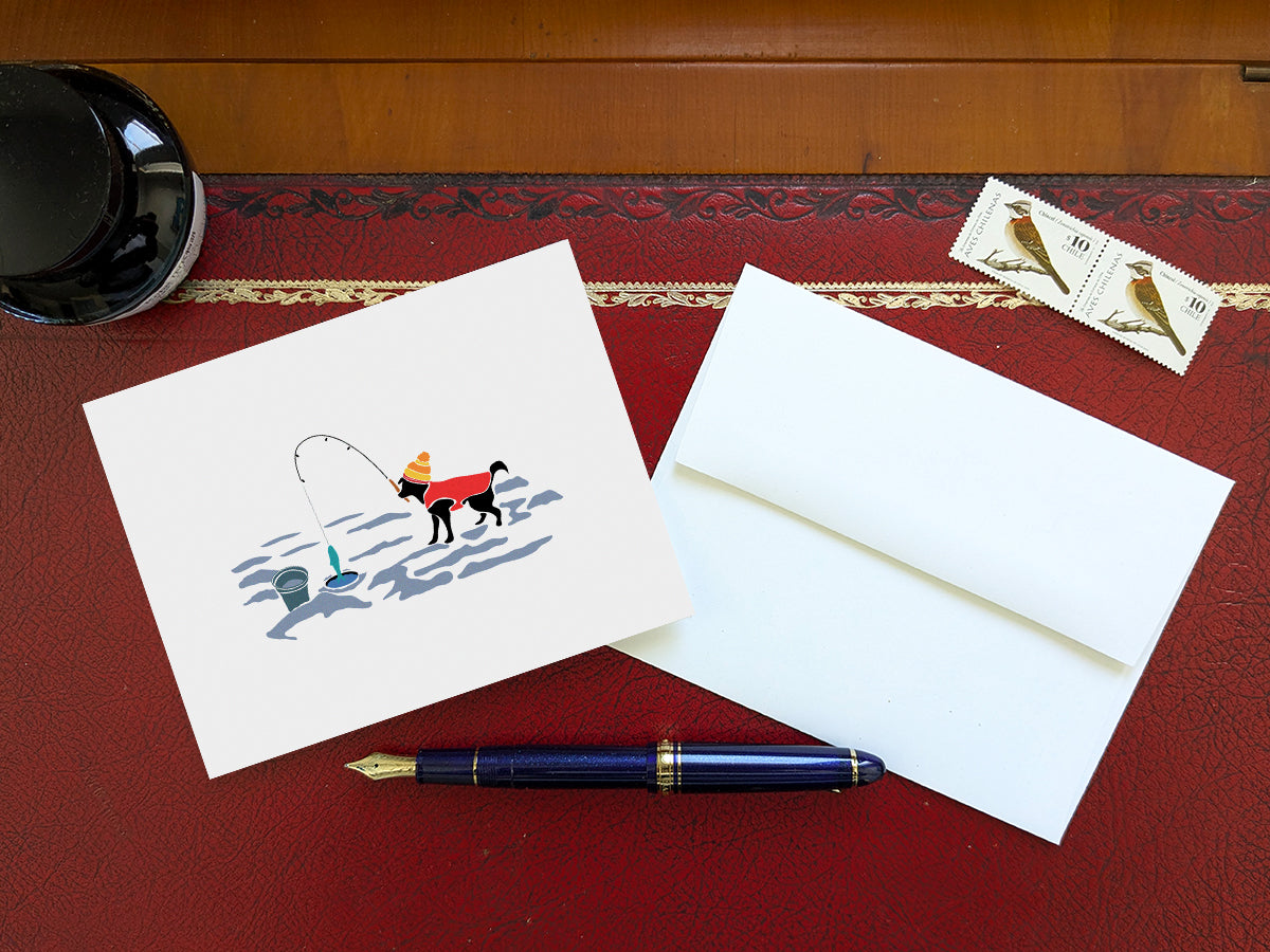 Greeting card with image of a dog with a winter hat and sweater ice fishing on a table with a blue pen and envelope and stamps.
