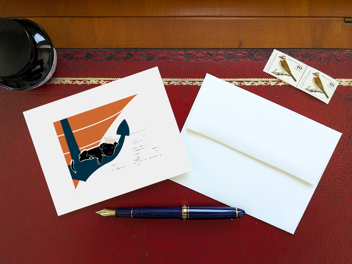 Greeting card with image of a dog sleeping on an anchor on a table with a blue pen and envelope and stamps.