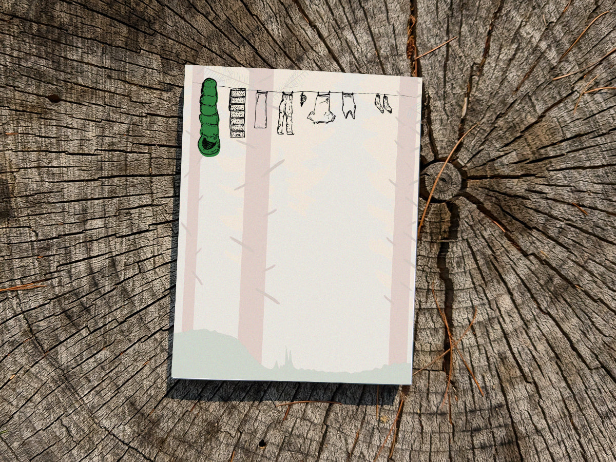 Notepad with clothes hanging on a line in a forest on wooden surface.