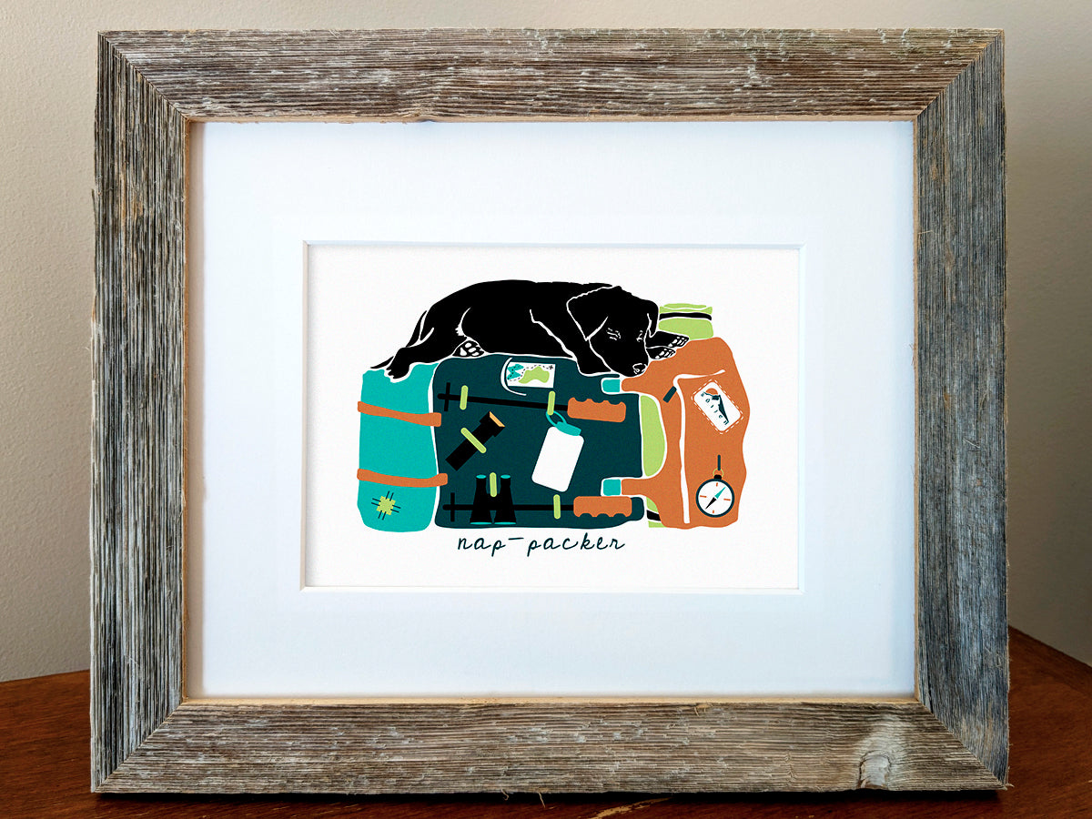 Framed art print of a black dog sleeping on top of a colorful backpack with the text nap-packer