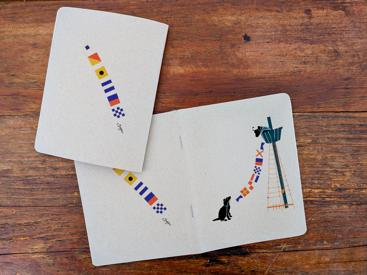 Two notebooks with dogs holding nautical flag illustration on a wooden surface