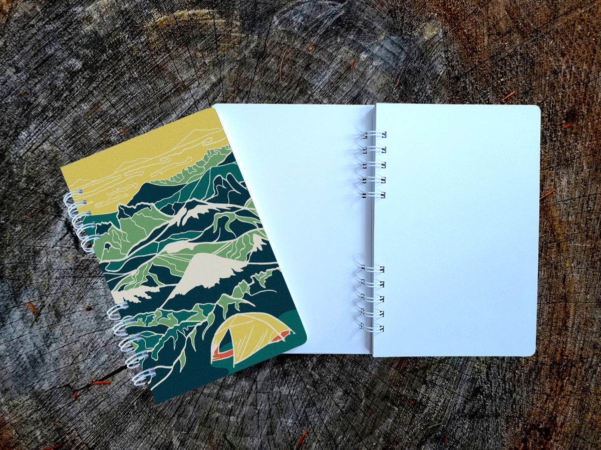 Notebook with illustration of a yellow tent among a background of blue and green mountains.