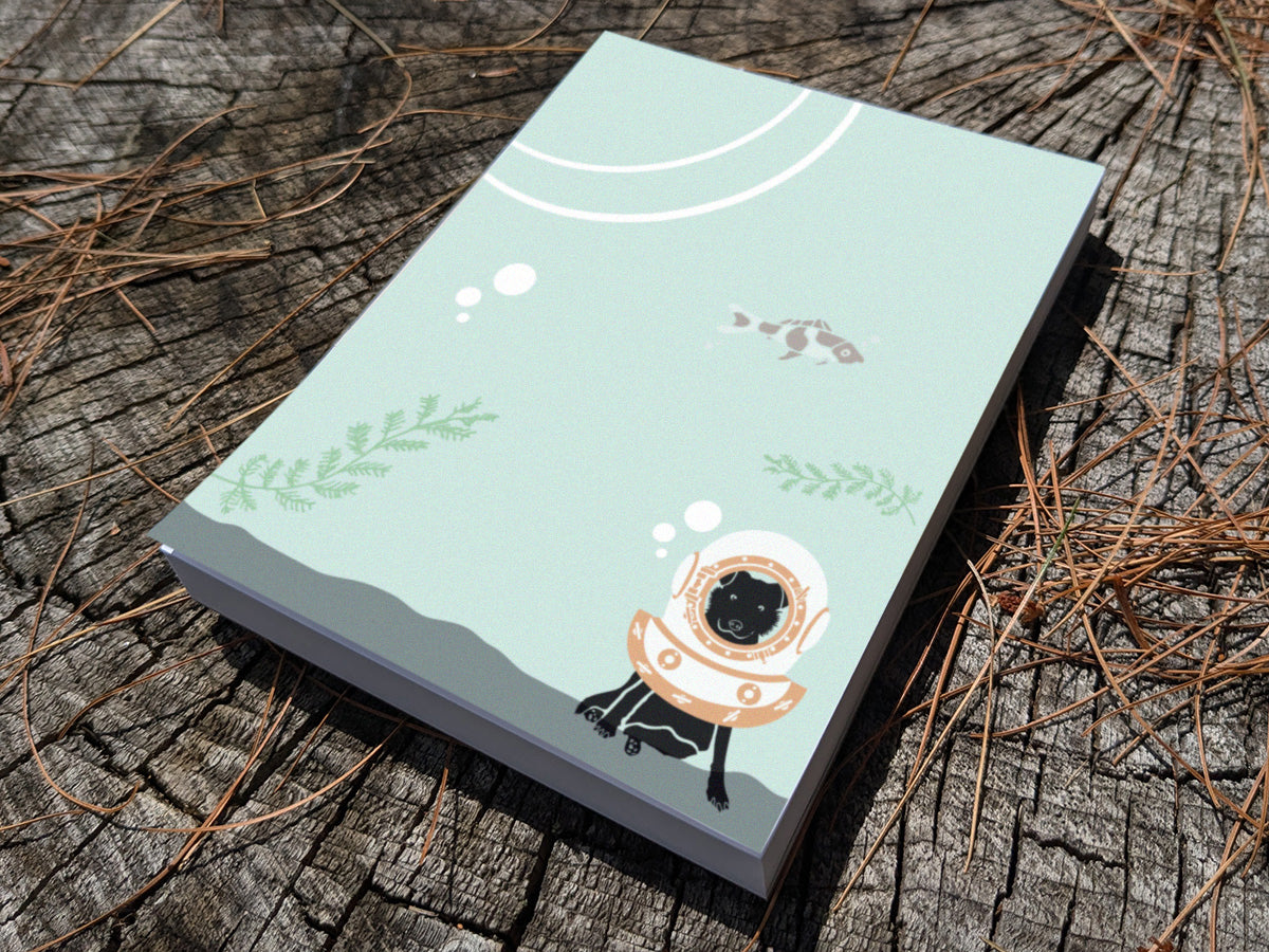 Notepad with a dog with old school diving helmet on a wooden surface.