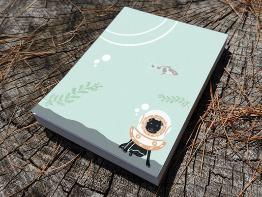 Notepad with a dog with old school diving helmet on a wooden surface.