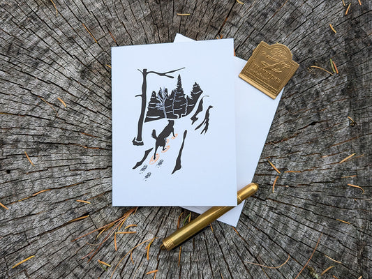 Greeting card with image of dog walking through forest wearing yellow snowshoes.