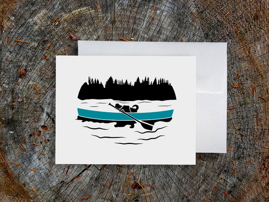 Greeting card with a black dog paddling a blue canoe with wood background