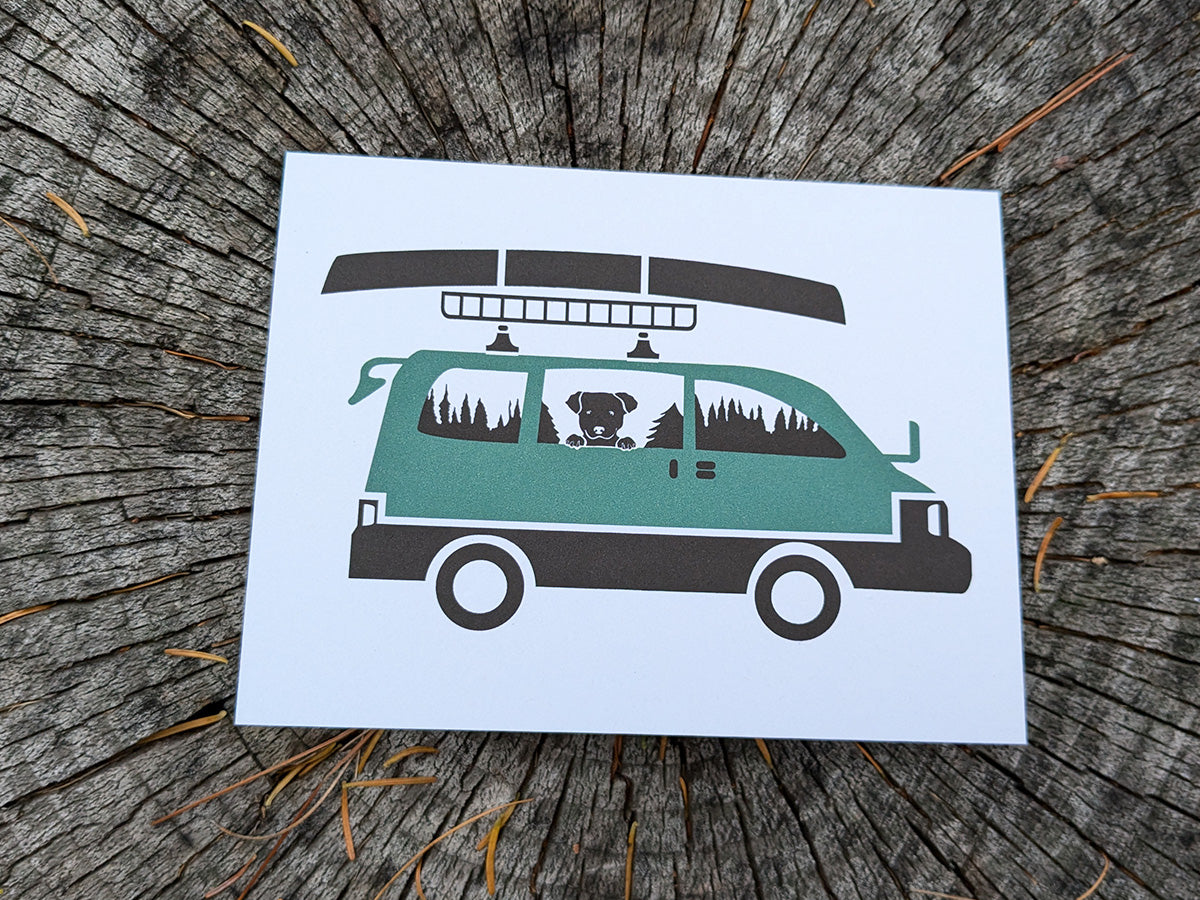 Greeting card with image of dog riding in a camper van with canoe on top.