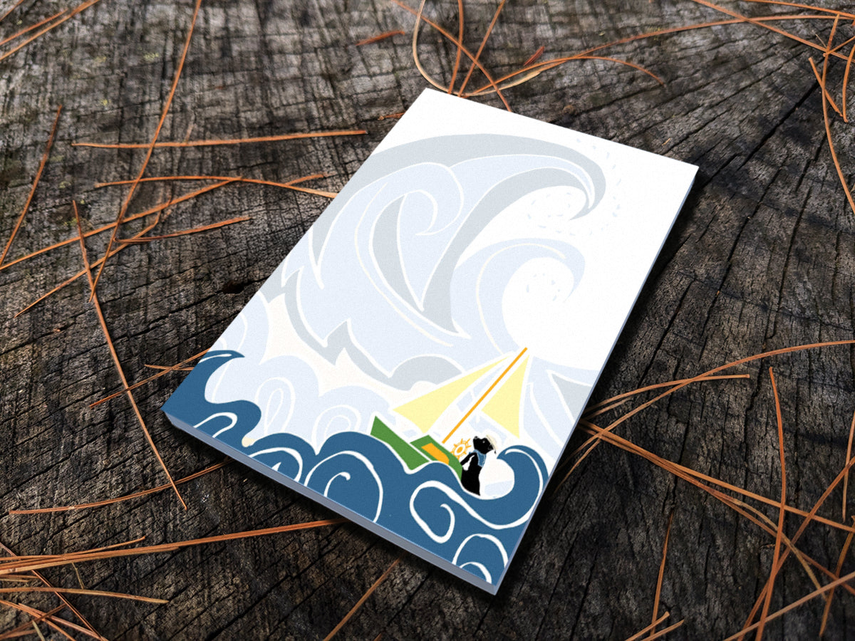 Notepad with illustration of dog sailing big waves on a wood surface.
