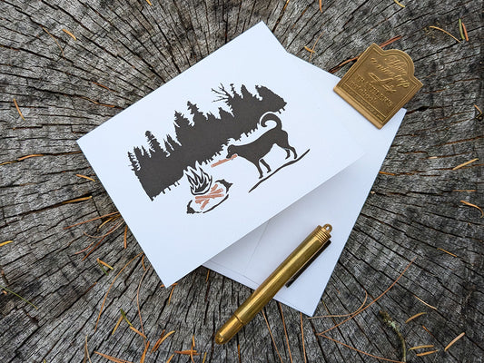 Greeting card with image of dog putting a log in a campfire.