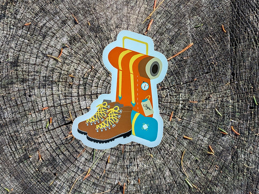 Sticker of hiking boot and backpack on a wooden background