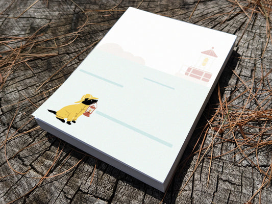 Notepad with an illustration of a dog in yellow hat and jacket holding a red lantern on a wood surface.