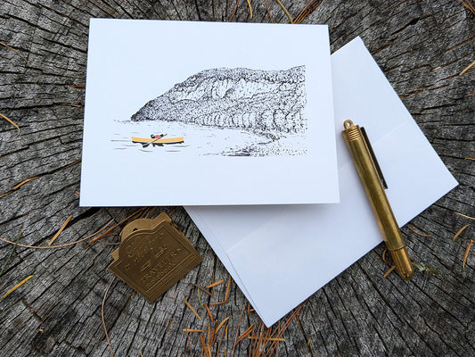 Greeting card featuring a dog paddling a canoe with mountain in the background.