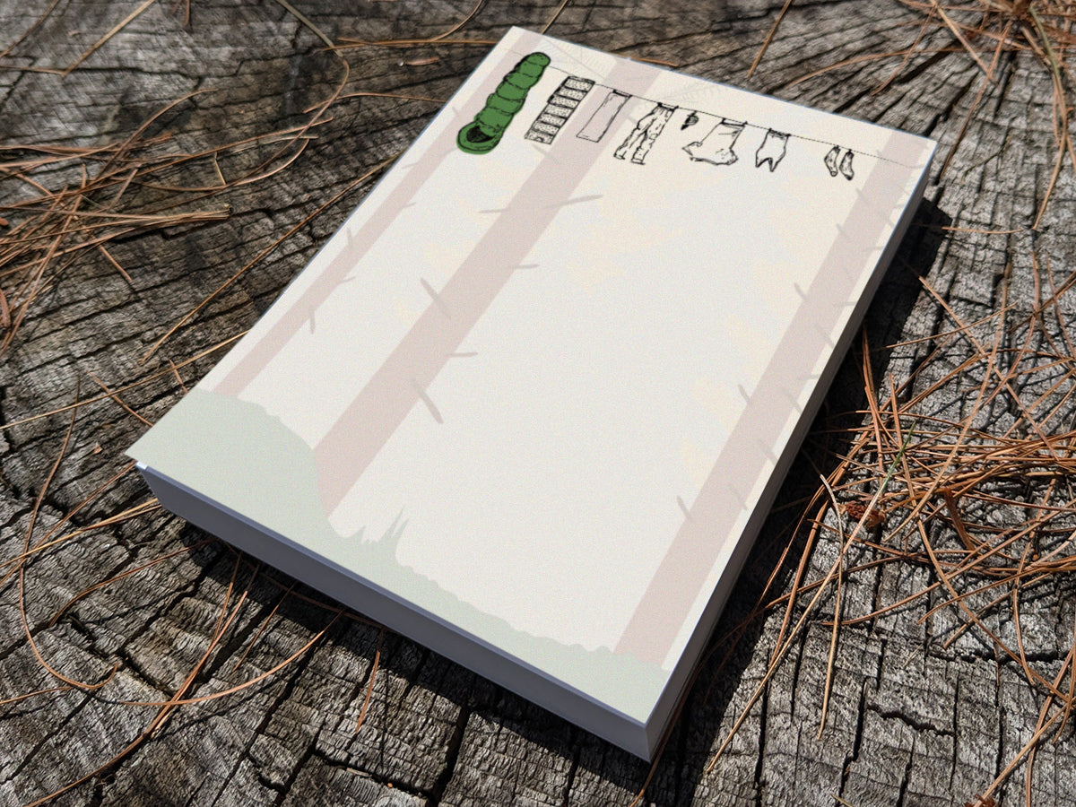 Notepad with clothes hanging on a line in a forest on wooden surface.
