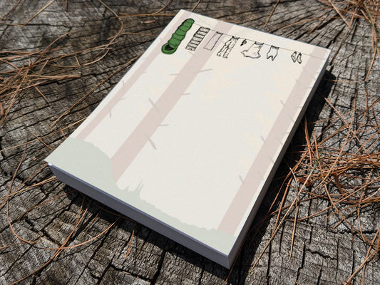Notepad with clothes hanging on a line in a forest on wooden surface.