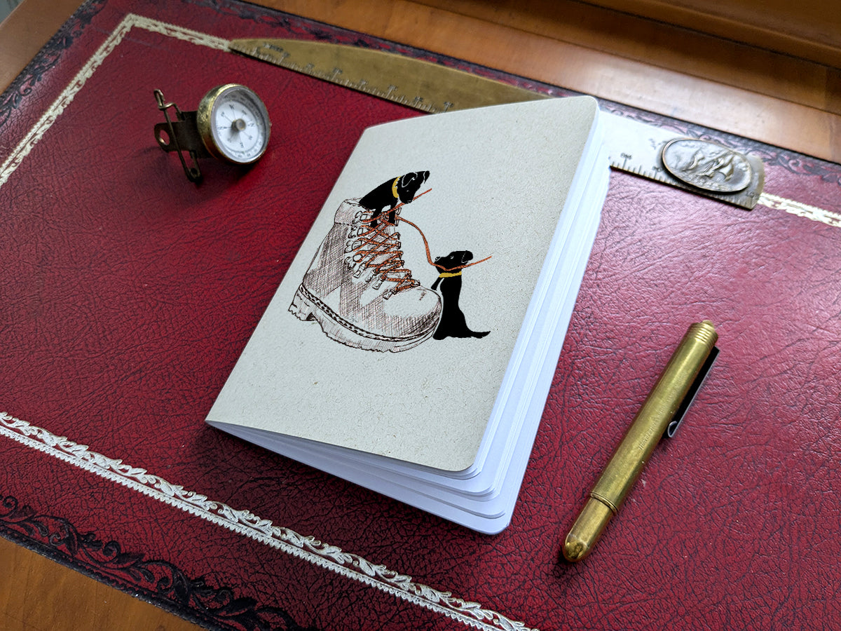 Notebook with dog and hiking boot illustration on a red surface with a pen and small compass.