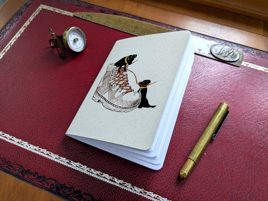Notebook with dog and hiking boot illustration on a red surface with a pen and small compass.