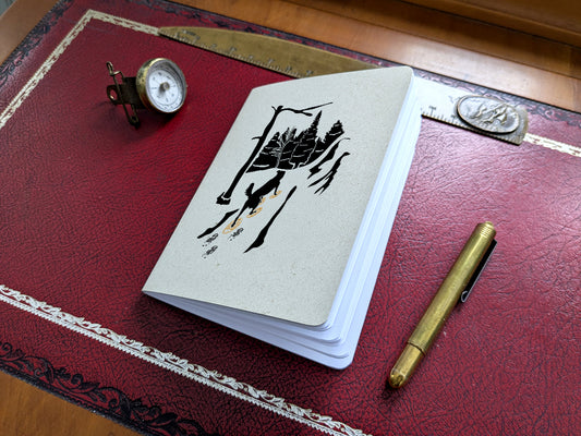 Notebook with dog snowshoeing illustration on a red surface with a pen and small compass.
