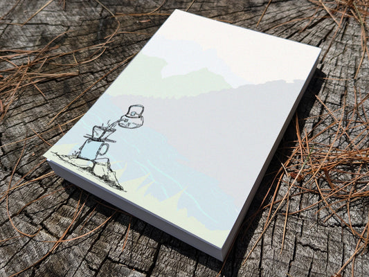 Notepad with illustration of pour-over coffee on a riverbank on a wood surface.