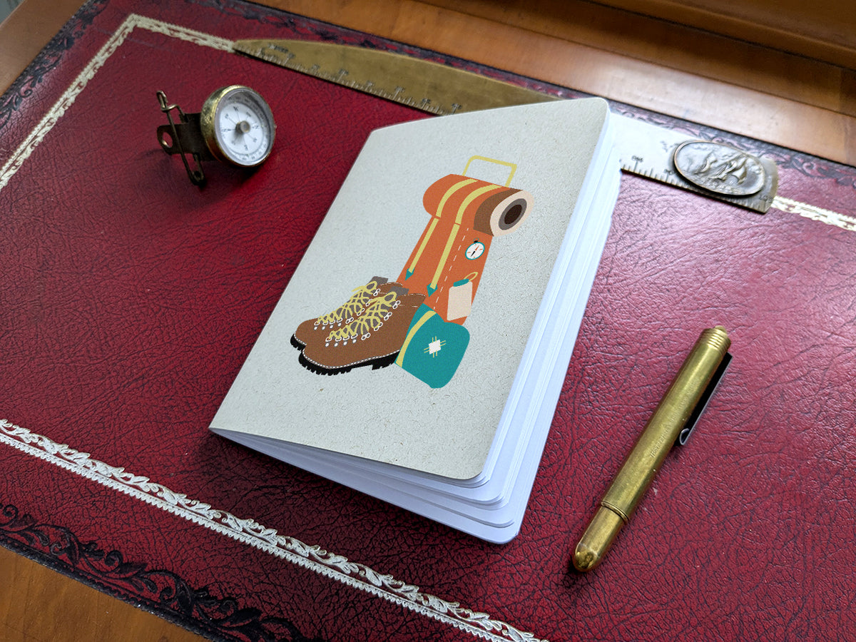 Notebook with hiking boot and backpack illustration on a red surface with a pen and small compass.
