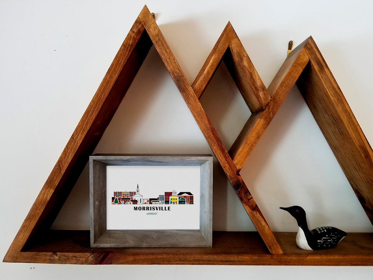 Framed art print on a wooden shelf of buildings arranged in a skyline with the text Morrisville Vermont