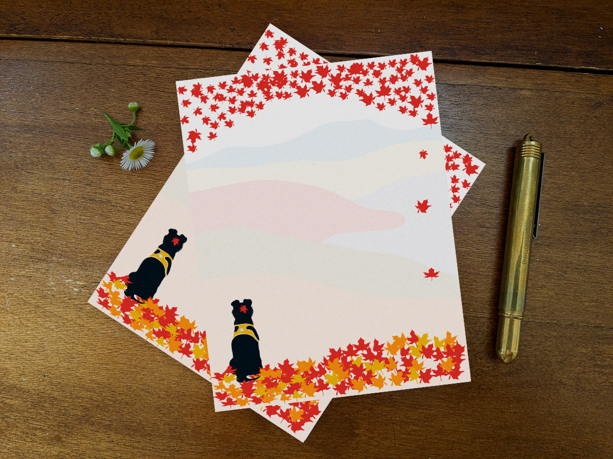 Notepad sheets with a black dog among fall foliage on wooden background and a gold pen.
