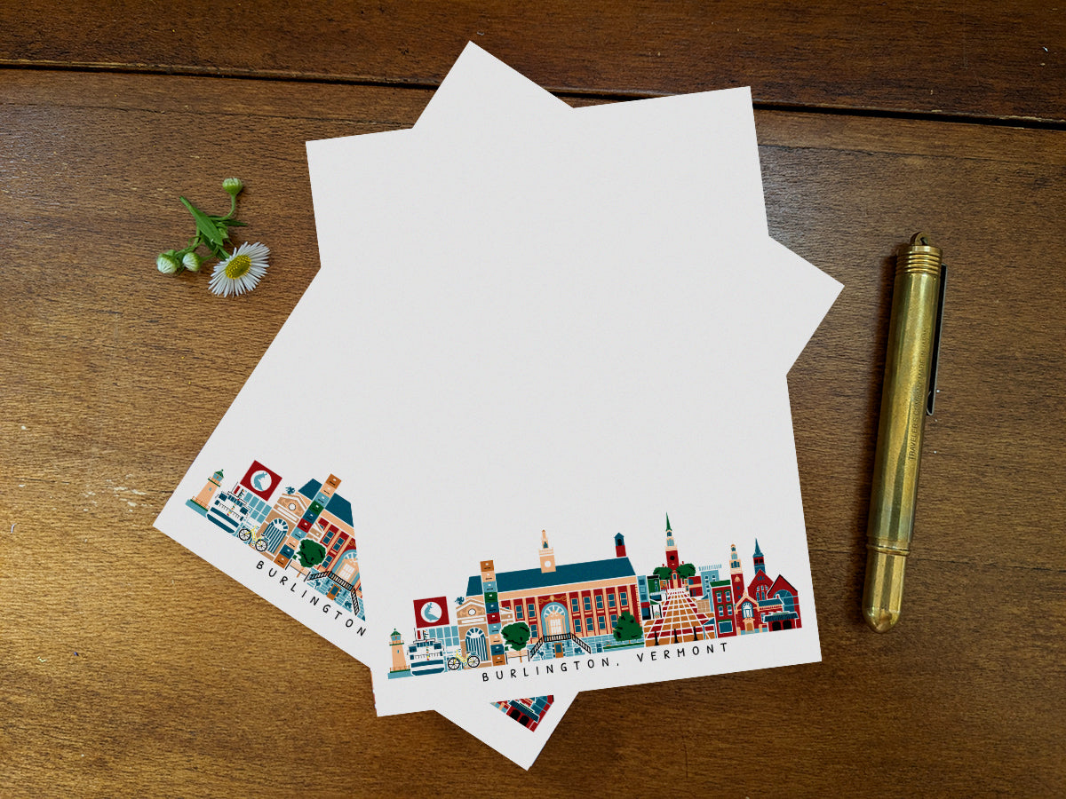 Notepad pages with illustration of Burlington, Vermont buildings in skyline on a wood surface with gold pen