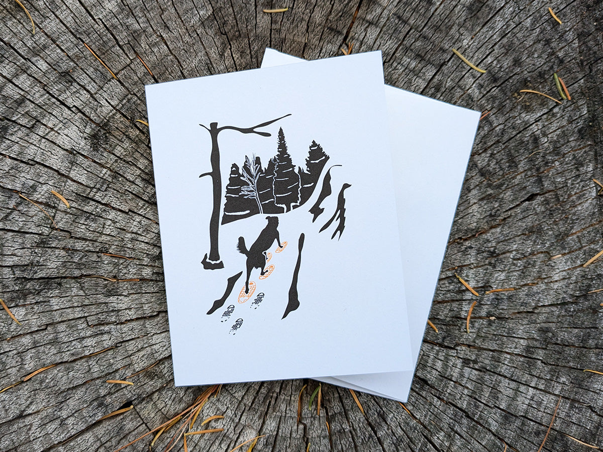 Greeting card with image of dog walking through forest wearing yellow snowshoes.