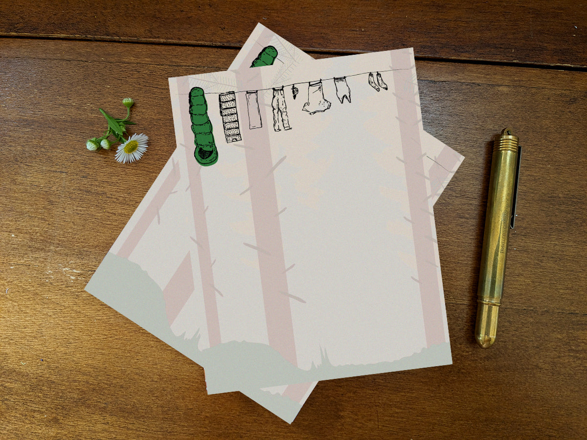 Notepad with clothes hanging on a line in a forest on wooden surface and gold pen.