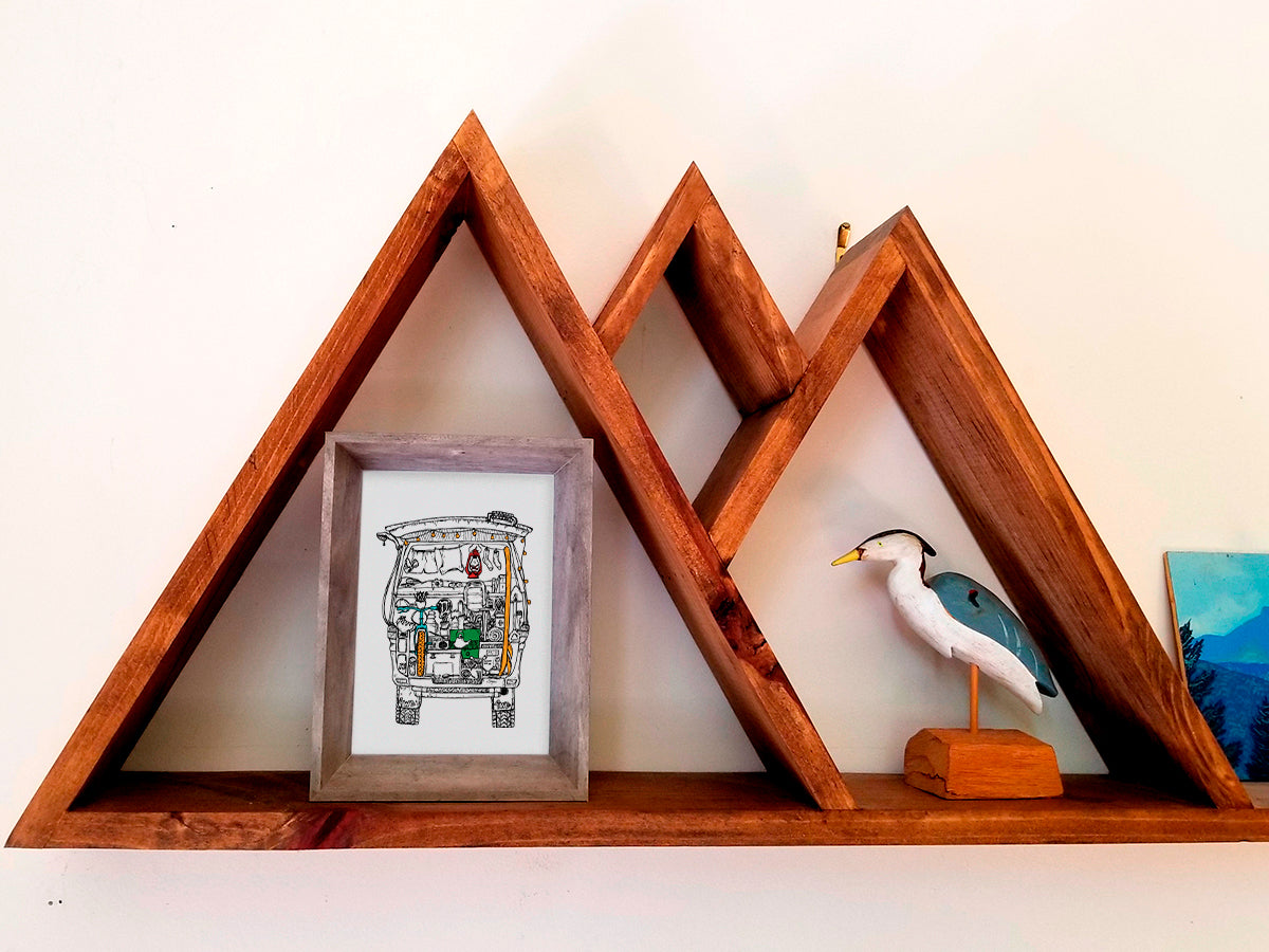 Framed illustration of a camper van filled with gear on a wood shelf.